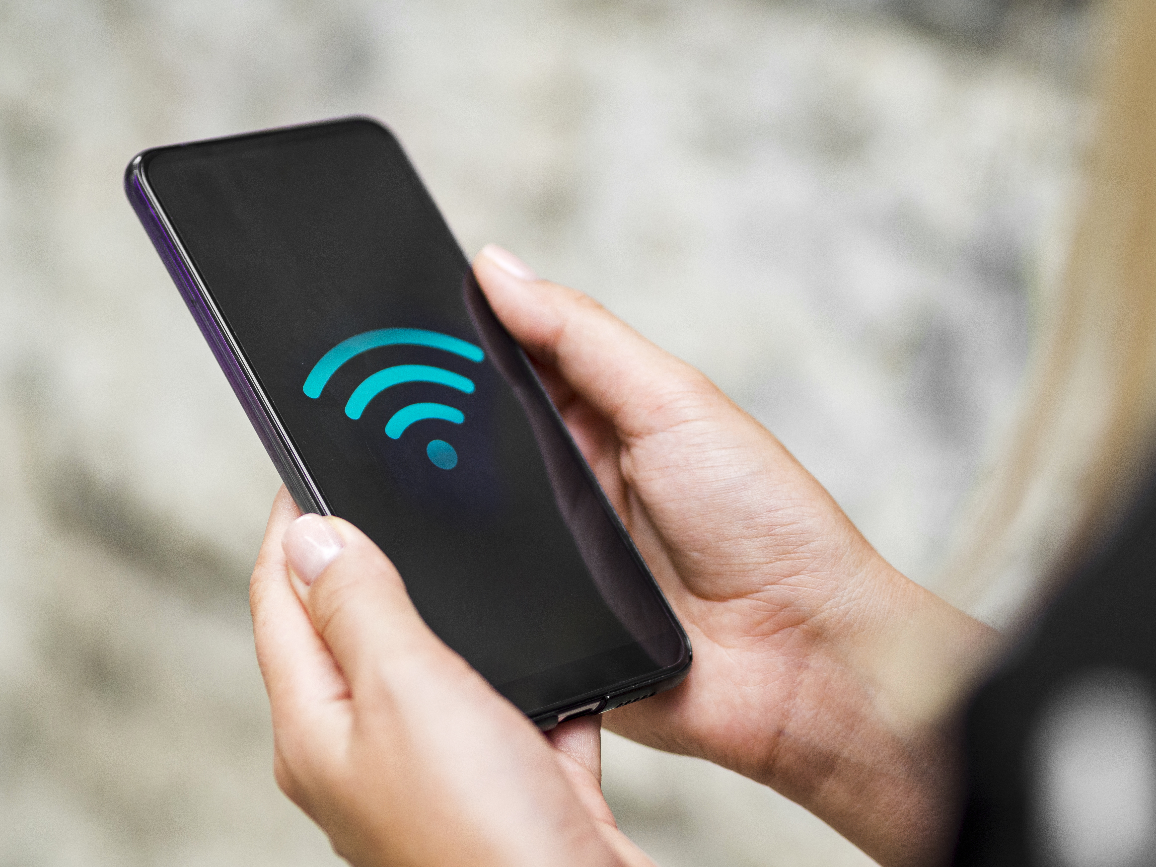 "Close-up of a smartphone in a person’s hand displaying a Wi-Fi symbol on the screen, to depict a solution for bad connection during rainy weather (koneksi jelek saat hujan).